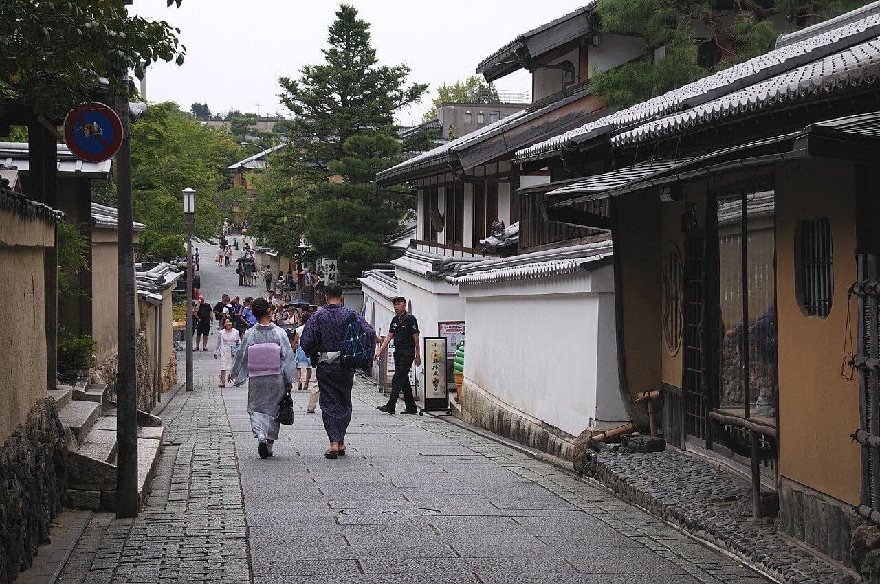 Pedestrians on a stone-paved street lined with traditional buildings in Gion, Kyoto.